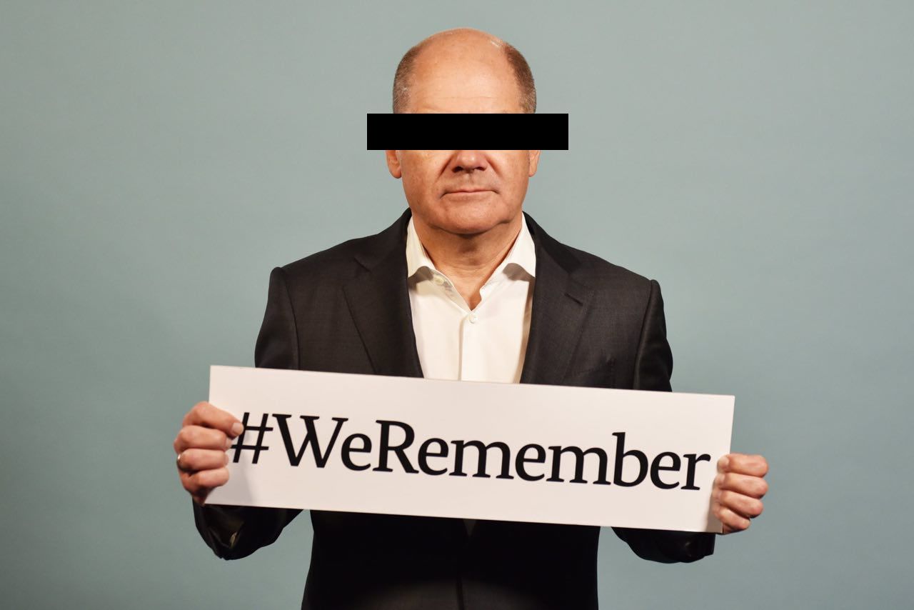 Olaf Scholz mit Querbalken vor Gesicht und #WeRemember Schild